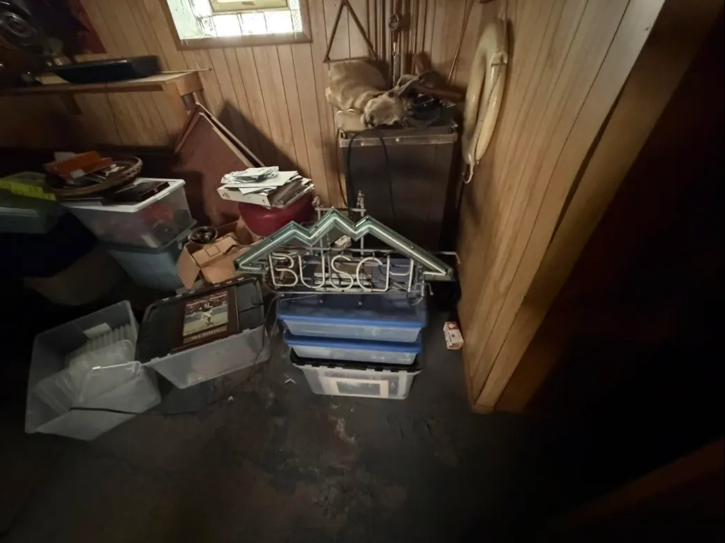 Wood-paneled basement corner stacked with bins, boxes and an old neon sign