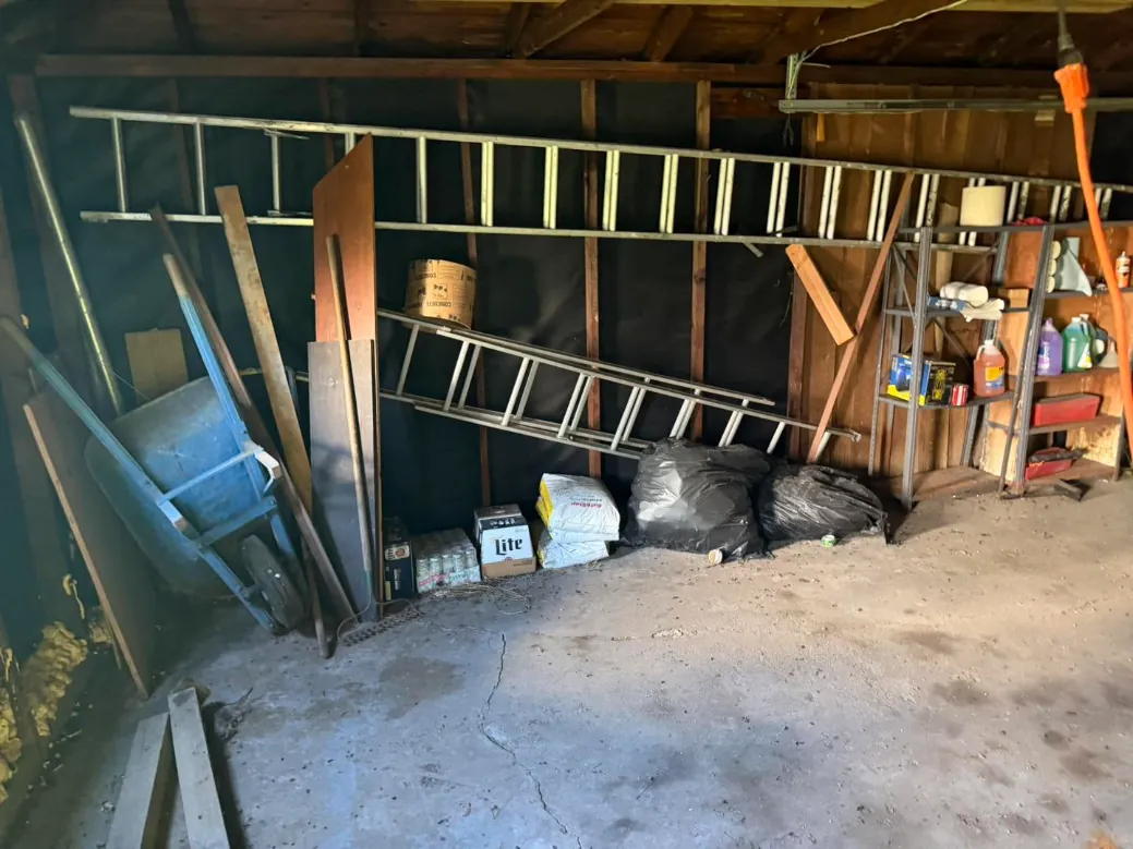 Cluttered garage with ladders, a wheelbarrow and bags of junk before a cleanout